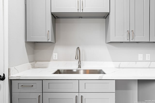 kitchen featuring gray cabinetry, light stone countertops, and sink