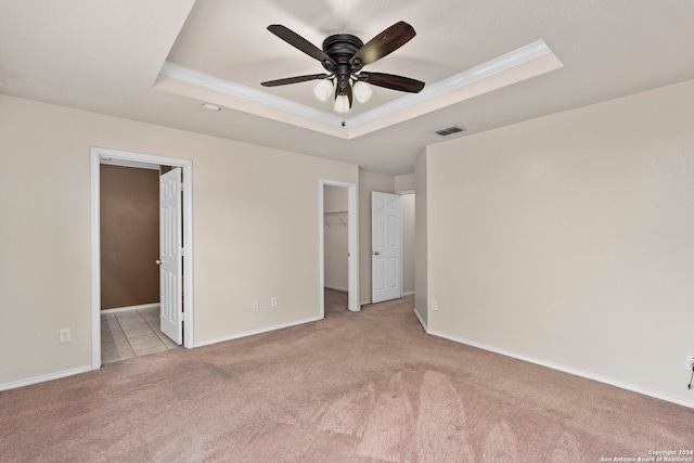 unfurnished bedroom with a tray ceiling, ceiling fan, a walk in closet, and light carpet