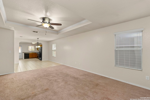 unfurnished living room with ceiling fan, a textured ceiling, a tray ceiling, crown molding, and light colored carpet