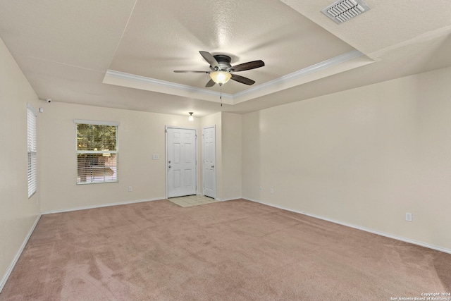 empty room with ceiling fan, light colored carpet, ornamental molding, and a tray ceiling