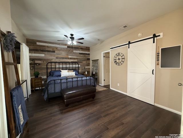 bedroom with wooden walls, a barn door, dark wood finished floors, and baseboards