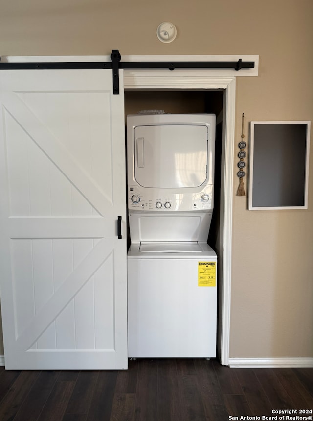laundry room featuring stacked washer and clothes dryer, dark wood-style floors, a barn door, and baseboards