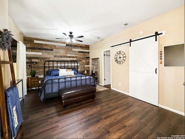 bedroom featuring wood walls, a barn door, dark hardwood / wood-style floors, and ceiling fan