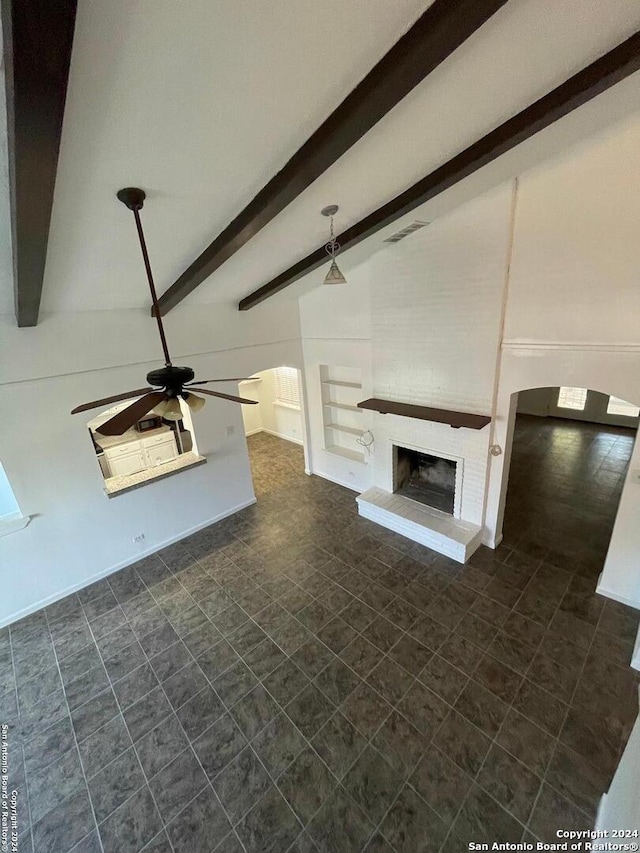 unfurnished living room featuring a brick fireplace, vaulted ceiling with beams, and ceiling fan