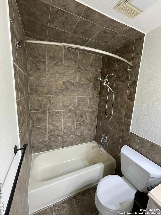 bathroom featuring tile walls, tiled shower / bath, and toilet