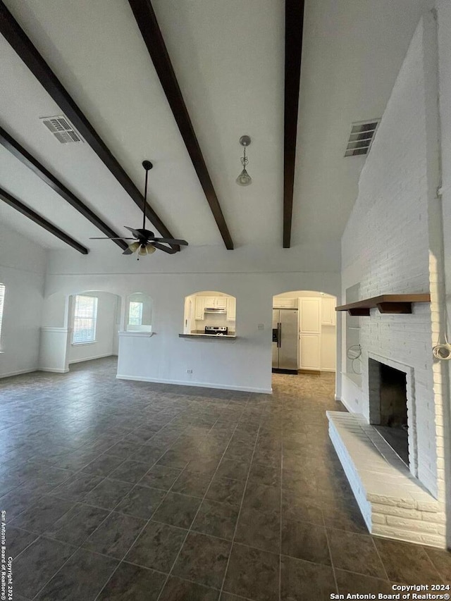 unfurnished living room featuring lofted ceiling with beams, dark tile patterned flooring, ceiling fan, and a brick fireplace