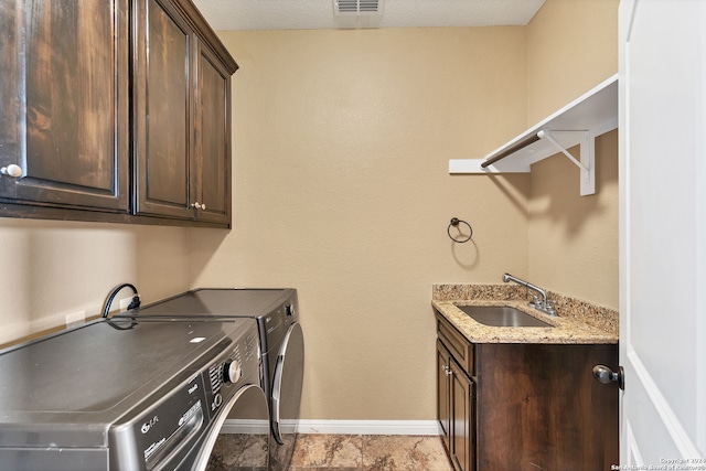 clothes washing area with cabinets, a textured ceiling, washing machine and dryer, and sink