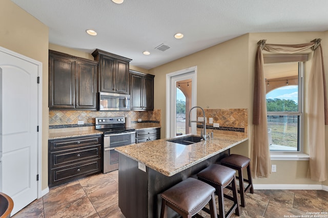 kitchen featuring stainless steel appliances, dark brown cabinetry, a center island with sink, sink, and a breakfast bar area