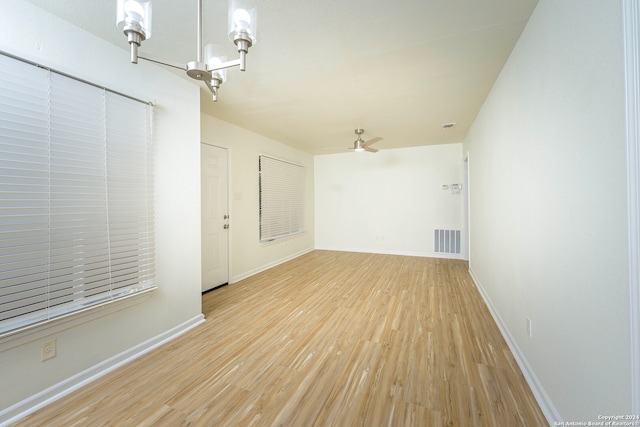 spare room with ceiling fan with notable chandelier and light wood-type flooring