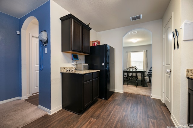 kitchen with dark wood-type flooring, black refrigerator, dark brown cabinetry, and light stone counters