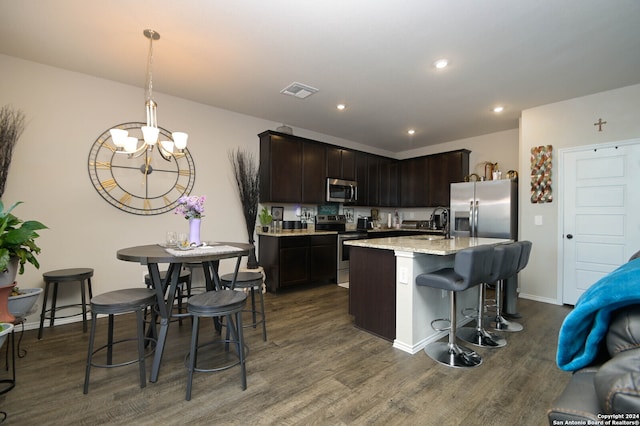 kitchen with stainless steel appliances, dark brown cabinetry, a center island with sink, dark hardwood / wood-style floors, and decorative light fixtures