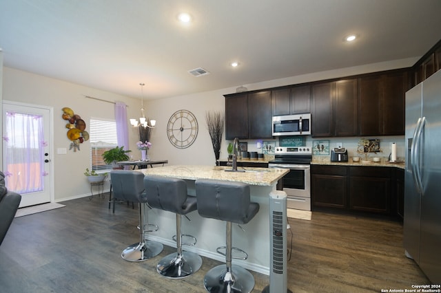 kitchen with a center island with sink, stainless steel appliances, dark hardwood / wood-style floors, pendant lighting, and light stone countertops