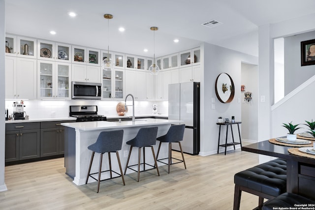 kitchen featuring pendant lighting, light wood-type flooring, stainless steel appliances, and a center island with sink