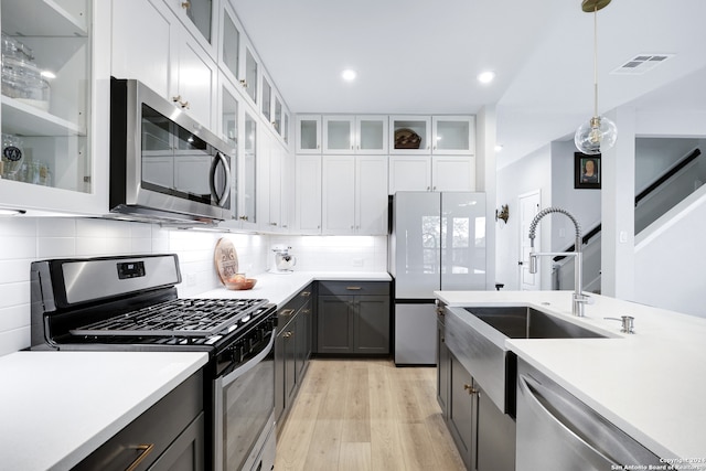 kitchen with white cabinets, sink, hanging light fixtures, light wood-type flooring, and stainless steel appliances