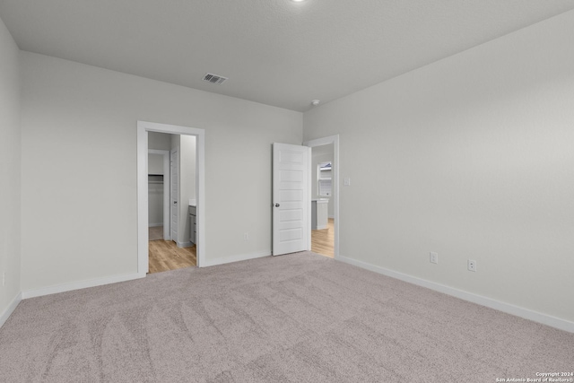 unfurnished bedroom featuring light colored carpet, a walk in closet, and a closet