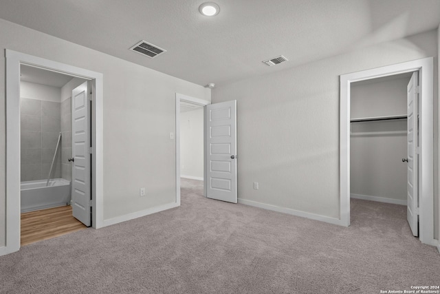 unfurnished bedroom featuring light carpet, a walk in closet, ensuite bath, and a closet