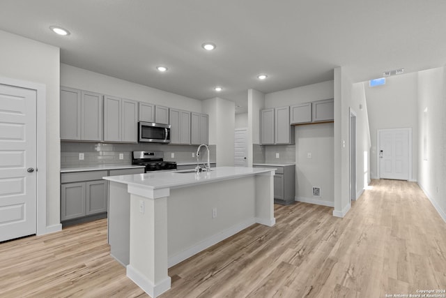 kitchen featuring gray cabinetry, sink, an island with sink, light hardwood / wood-style floors, and appliances with stainless steel finishes