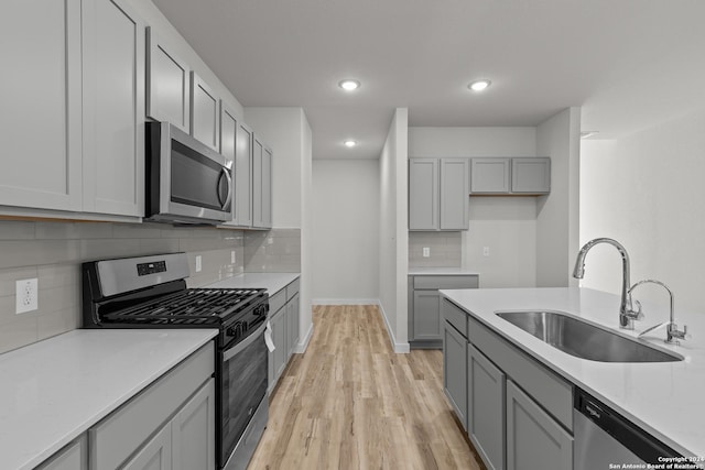 kitchen featuring appliances with stainless steel finishes, tasteful backsplash, sink, light hardwood / wood-style flooring, and gray cabinets