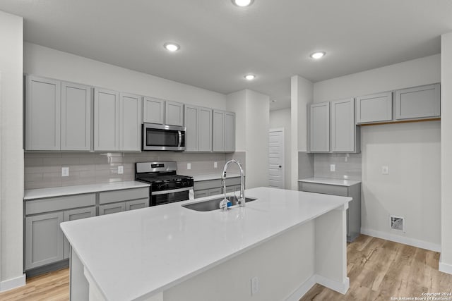 kitchen with light hardwood / wood-style floors, sink, stainless steel appliances, and an island with sink