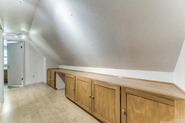 bonus room featuring lofted ceiling, light wood-type flooring, and a textured ceiling