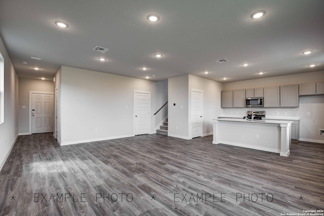 kitchen with gray cabinets, dark hardwood / wood-style flooring, stainless steel appliances, and a kitchen island with sink