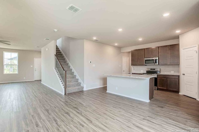 kitchen featuring sink, appliances with stainless steel finishes, an island with sink, dark brown cabinets, and light hardwood / wood-style flooring