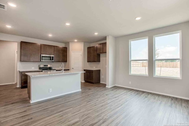 kitchen with stainless steel appliances, light hardwood / wood-style floors, sink, and a kitchen island with sink