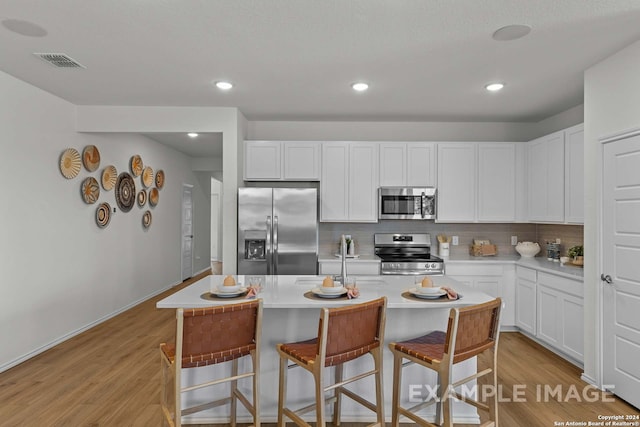 kitchen featuring a center island with sink, a kitchen breakfast bar, white cabinets, light hardwood / wood-style floors, and stainless steel appliances