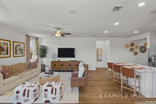 living room featuring a textured ceiling, light hardwood / wood-style flooring, and ceiling fan