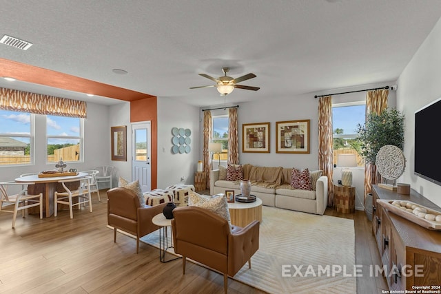 living room with ceiling fan, plenty of natural light, a textured ceiling, and light wood-type flooring