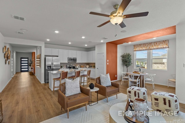 living room featuring light hardwood / wood-style flooring, ceiling fan, and sink