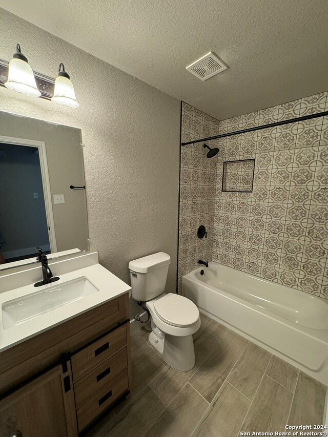 full bathroom featuring vanity, a textured ceiling, toilet, and tiled shower / bath