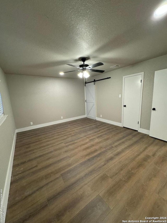 unfurnished bedroom featuring a barn door, ceiling fan, dark hardwood / wood-style flooring, and a textured ceiling