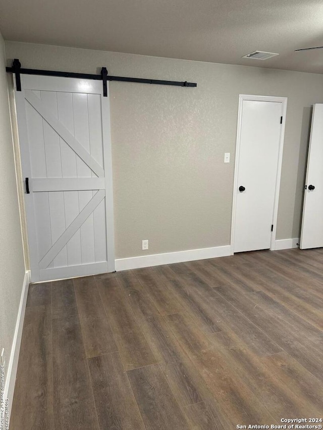 unfurnished room with a barn door and dark wood-type flooring