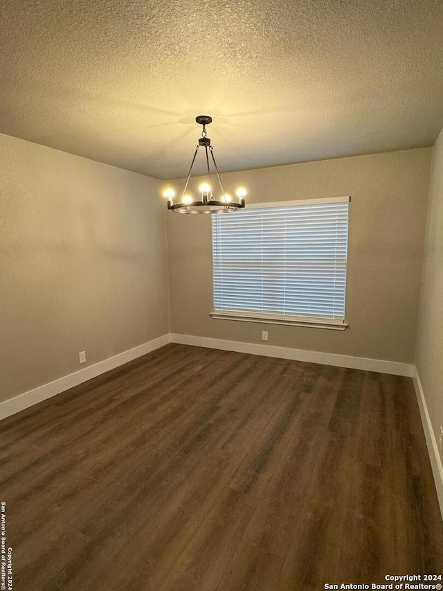 unfurnished room with dark hardwood / wood-style floors, a textured ceiling, and an inviting chandelier