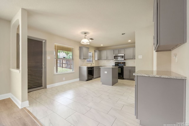 kitchen with sink, appliances with stainless steel finishes, light stone countertops, a center island, and gray cabinetry