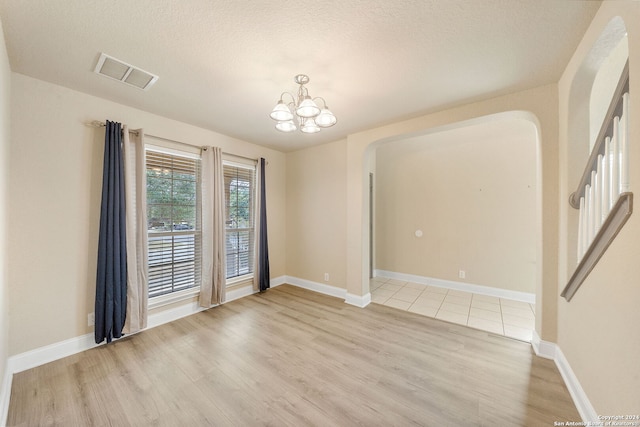 empty room with a textured ceiling, light hardwood / wood-style flooring, and a chandelier