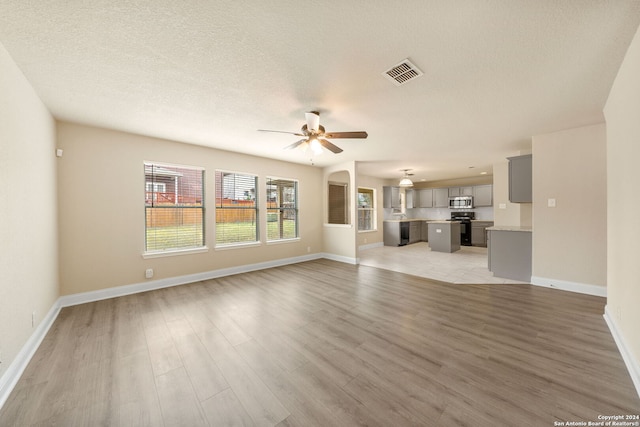 unfurnished living room featuring ceiling fan, a textured ceiling, and light hardwood / wood-style floors