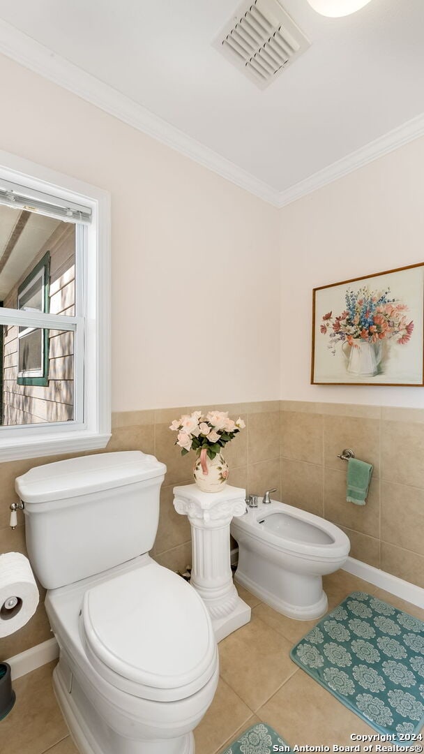 bathroom with a bidet, tile patterned flooring, crown molding, toilet, and tile walls