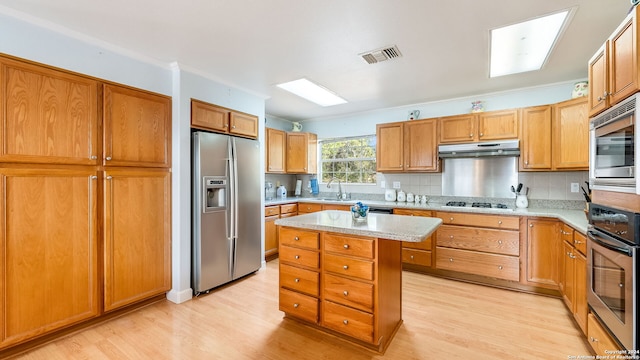 kitchen featuring ornamental molding, stainless steel appliances, a kitchen island, decorative backsplash, and light hardwood / wood-style floors