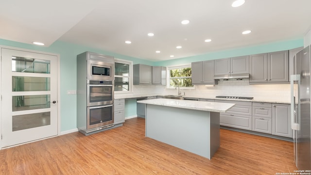 kitchen featuring appliances with stainless steel finishes, light hardwood / wood-style floors, light stone countertops, and a kitchen island