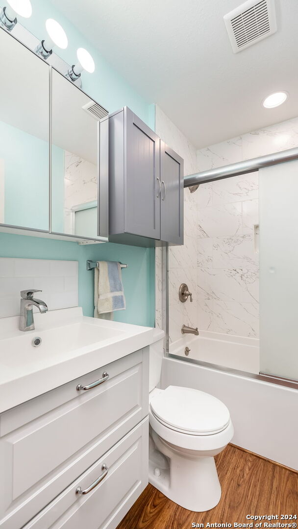 full bathroom featuring wood-type flooring, shower / bath combination with glass door, backsplash, vanity, and toilet