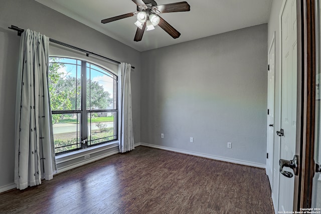 empty room with dark wood-type flooring, ceiling fan, and a healthy amount of sunlight