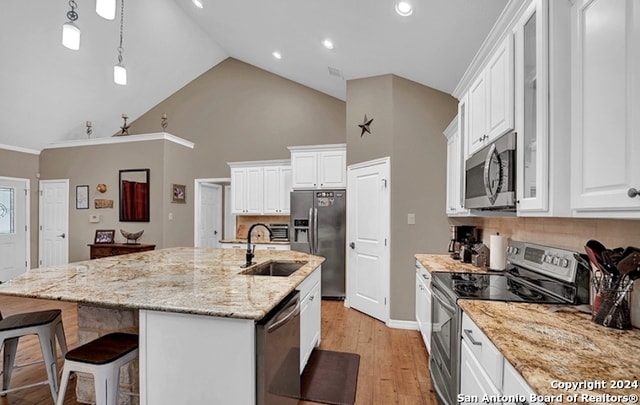 kitchen with a center island with sink, stainless steel appliances, white cabinetry, light wood-type flooring, and high vaulted ceiling