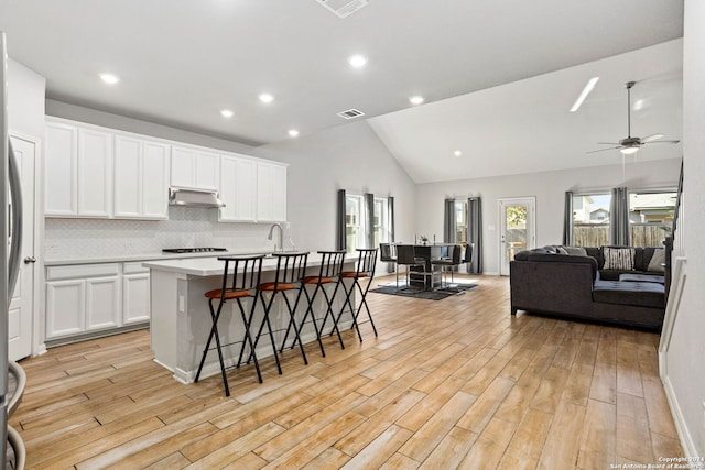 kitchen featuring white cabinets, vaulted ceiling, an island with sink, and light hardwood / wood-style flooring