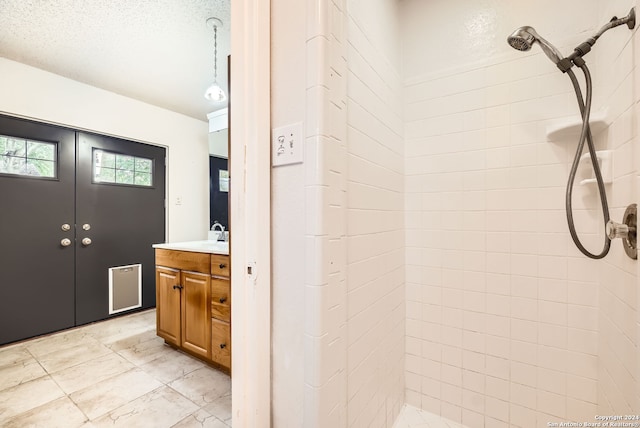 bathroom featuring a textured ceiling, vanity, and tiled shower