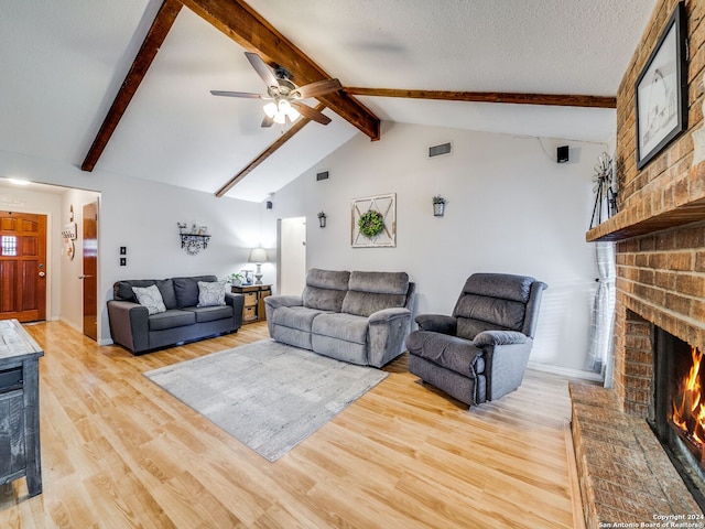 living room with ceiling fan, a textured ceiling, light hardwood / wood-style flooring, vaulted ceiling with beams, and a brick fireplace