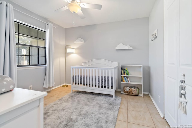 bedroom featuring ceiling fan, light tile patterned floors, and a crib