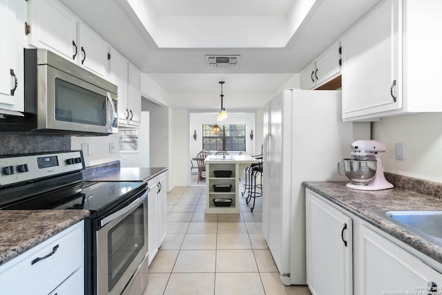 kitchen featuring stainless steel appliances, a raised ceiling, light tile patterned floors, decorative light fixtures, and white cabinetry