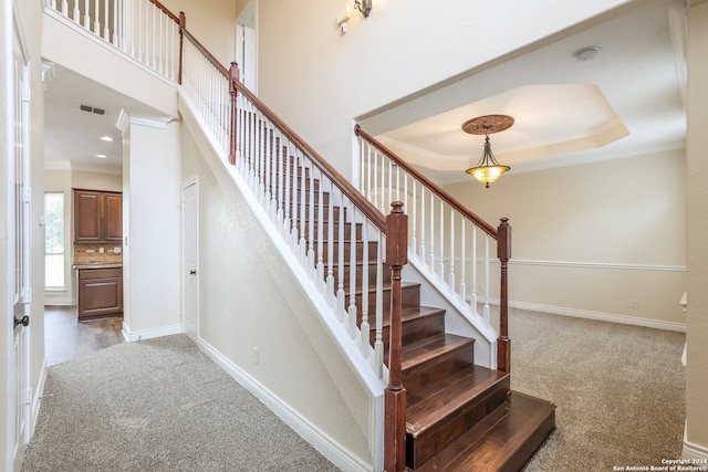 stairway with a raised ceiling, crown molding, and carpet